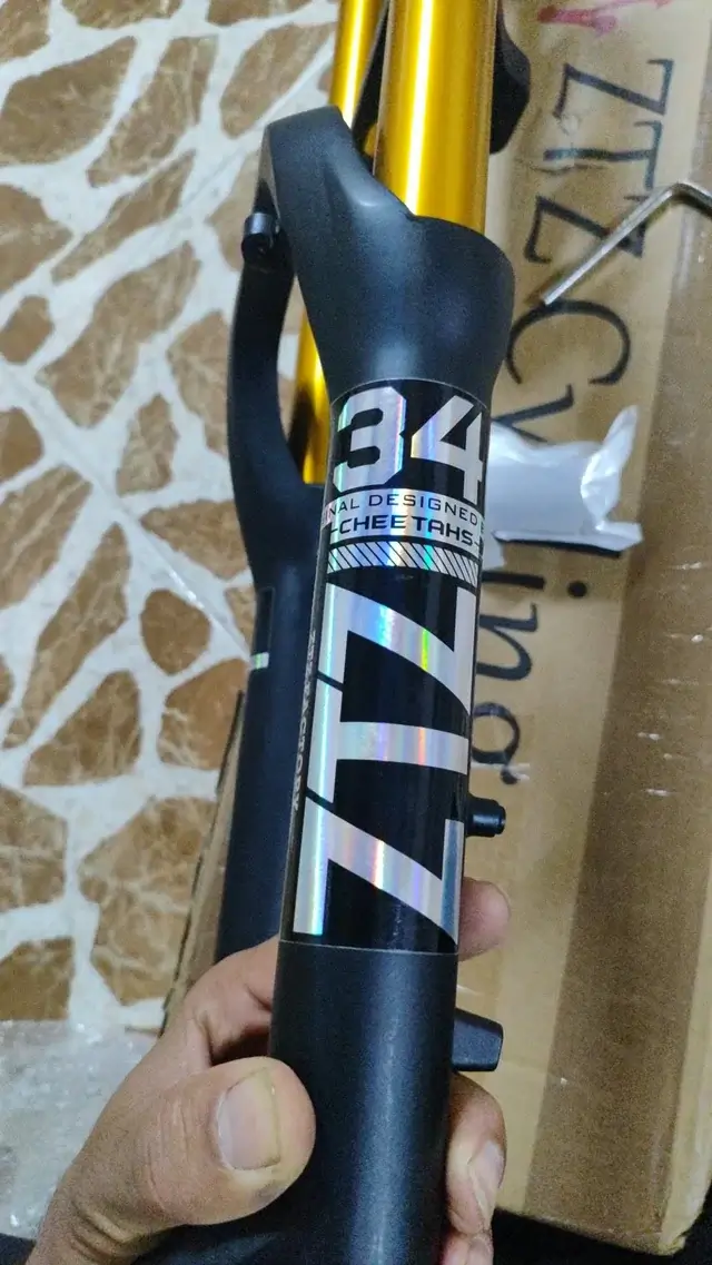 A hand holding a gold-stanchion ZTZ air suspension fork in front of its shipping box